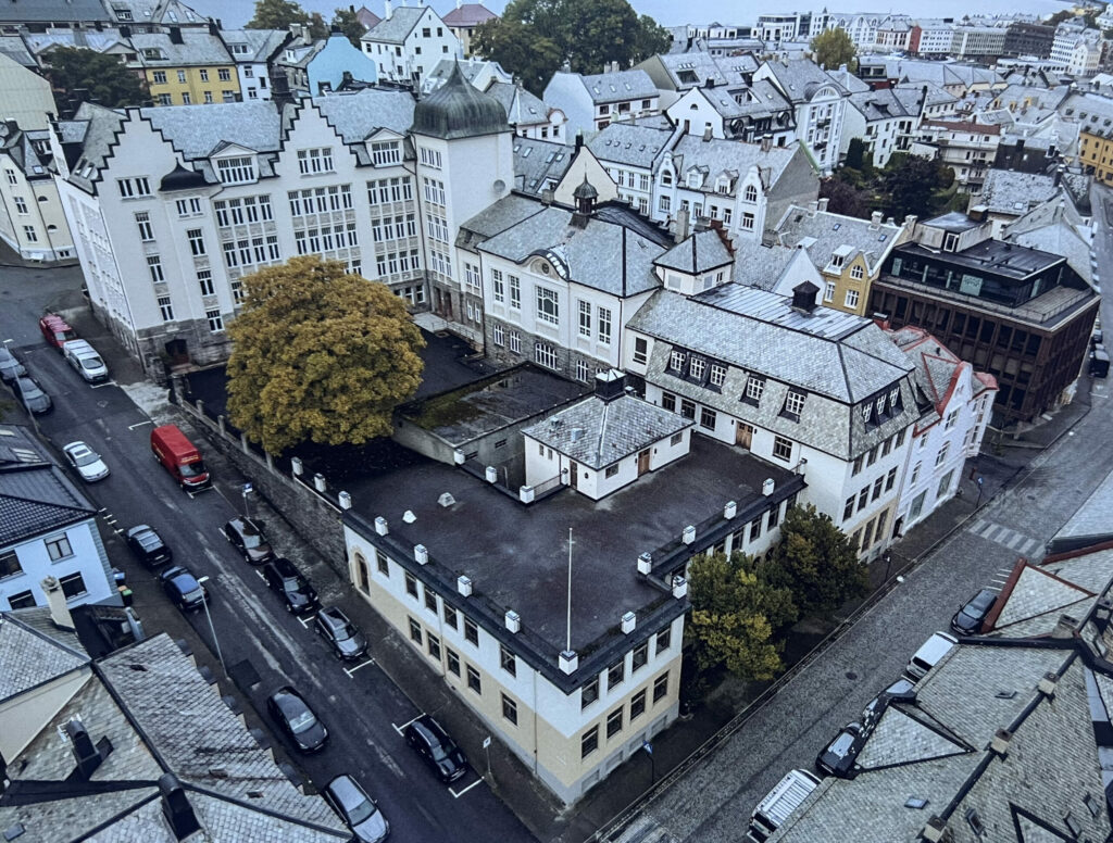 Dette bildet er tatt fra lufta i oktober 2024, og er henta fra boka «Latinskolen i Ålesund», som kom ut i fjor. Det er i den bygninga som ligger omtrent midt på bildet, med tårn og spir på taket, som huser sløydsalen i første etasje. (Gymnastikksalen i etasjen over.) Her på «sløyden» var det de to siste brødfjølene blei produsert. De seks andre blei laga på sløyden på Aspøyskolen, litt lenger ute på Aspøya. Foto: Vasco Pinhol.